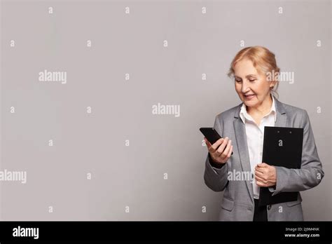 Adult Mature Woman Wearing Suit And Shirt Holding Cellphone Over Gray