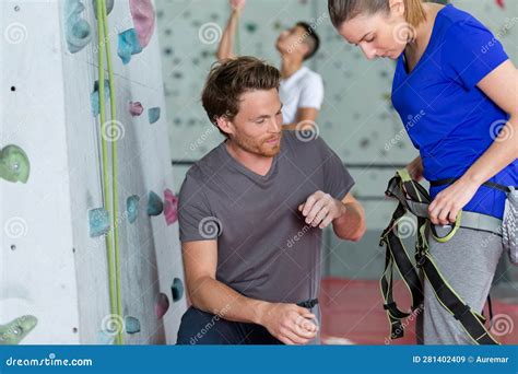 Instructor Attaching Rope To Climber At Indoor Wall Climbing Center