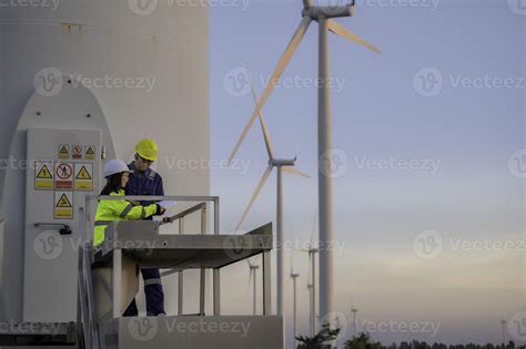 Two Engineers Working And Holding The Report At Wind Turbine Farm Power Generator Station On