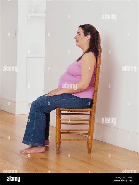 Pregnant Woman Sitting Upright In Chair Hands Resting On Her Knees