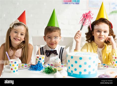 Los niños con gorros de fiesta sentado en la mesa y mirando a la cámara