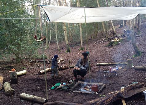 Two People Cooking Food Over An Open Fire In The Middle Of A Forest