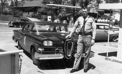 an old black and white photo of a man standing in front of a car at a ...