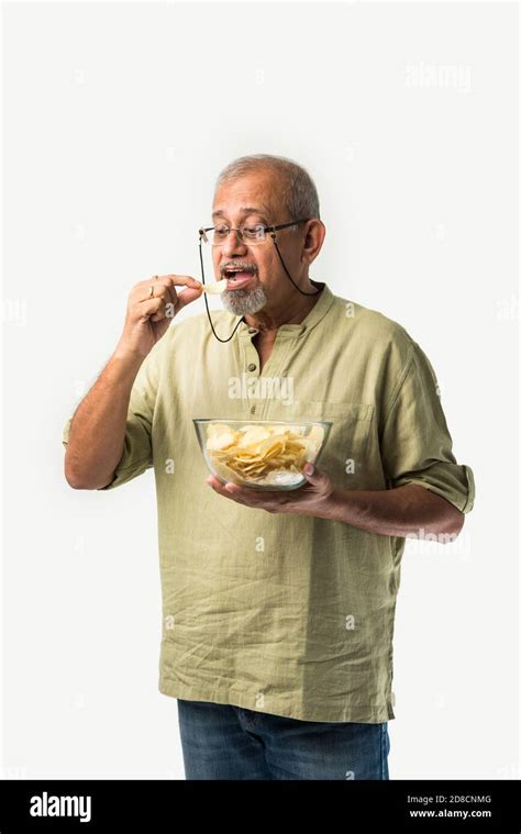 Indian Asian Old Or Retired Senior Man Eating Potato Chips On White