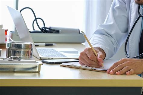 Premium Photo Midsection Of Doctor Writing On Paper At Table In Hospital