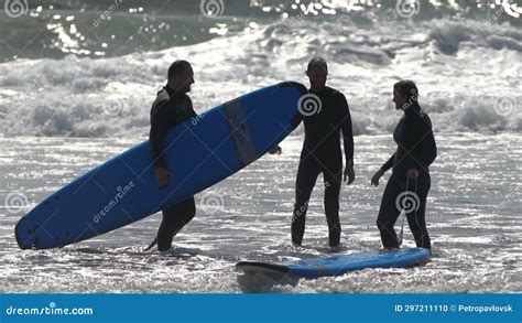 Surfers Woman And Two Men In Wetsuits With Surfboards Cheerfully