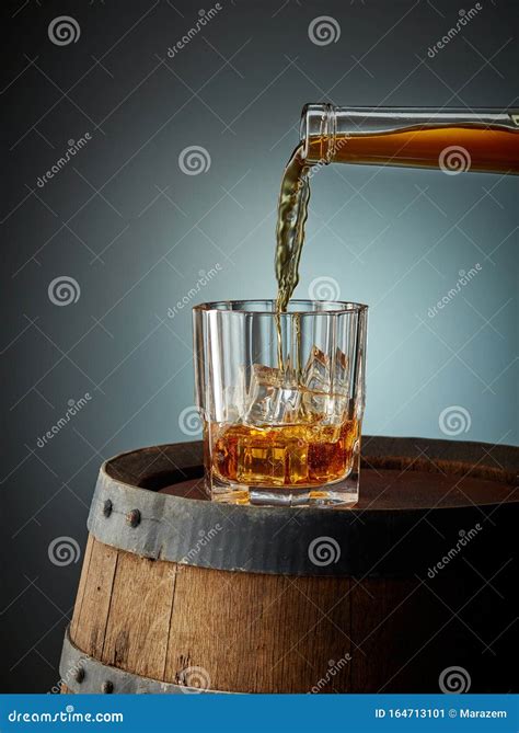 Whiskey Pouring Into Glass With Ice Isolated On Black Background