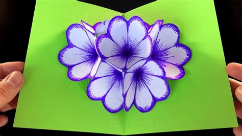 Two Hands Holding An Open Card With Purple Flowers On Green Paper In