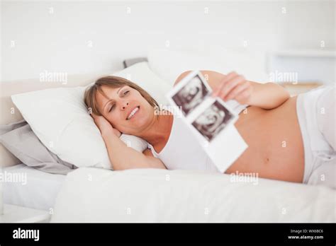 Pretty Pregnant Woman Holding An Ultrasound Scan While Lying On Her Bed