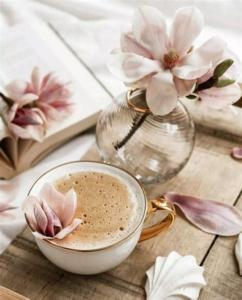 A Cup Of Coffee And Some Flowers On A Wooden Table Next To An Open Book