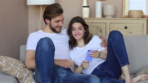 Happy Couple Sitting And Planning New Home Decoration At Home With A Smartphone Stock Footage