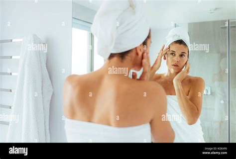 Woman Massaging Her Face Looking At A Mirror In Bathroom Woman In Towels Wrapped Around Head