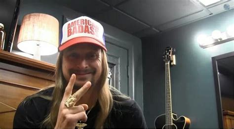 A Man With Long Hair Wearing A Hat And Making The Peace Sign In Front