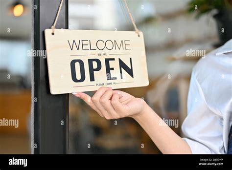 Female barista holding a coffee shop welcome sign in front of the coffee shop. close-up image ...