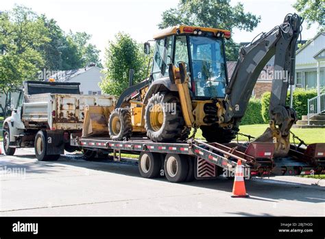 A Dump Truck Delivers A Front End Loader Back Hoe On A Trailer To A