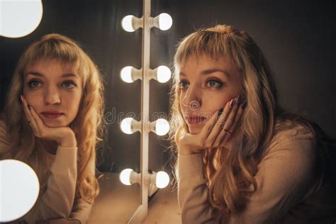 La Fille Blonde Regarde Dans Le Miroir Entouré Par Des Lumières Image