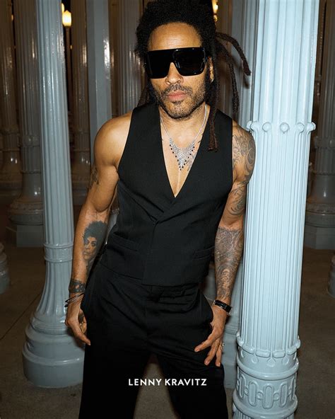 a man with dreadlocks and sunglasses standing in front of some white pillars wearing a black outfit