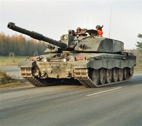 an army tank driving down the road with two people on it's back end