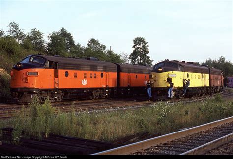 An Orange And Yellow Train Traveling Down Tracks Next To Another Train