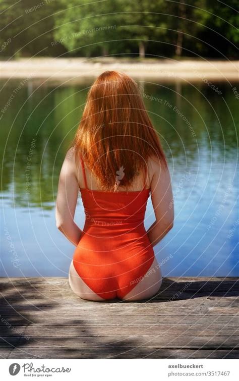 Rear View Woman Wearing Red Bathing Suit Sitting On Wooden Pier A