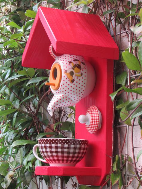 A Red Birdhouse With A Bowl And Cup On The Shelf In Front Of It