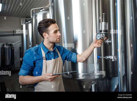 Brewery Worker Checking Fermentation Process In Steel Vat And Look At