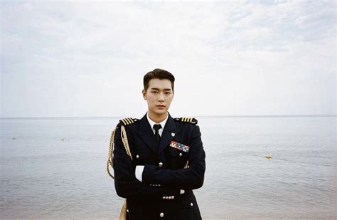 A Man In Uniform Standing On The Beach With His Arms Crossed And