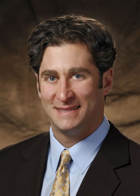 A Man In A Suit And Tie Smiling At The Camera With A Brown Backdrop