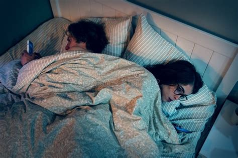 Husband And Wife Lie In Bed Facing Away From Each Other Looking At