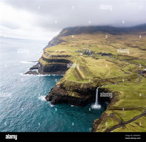 Scenic View Of Mulafossur Waterfall With Mountain And Sea Stock Photo