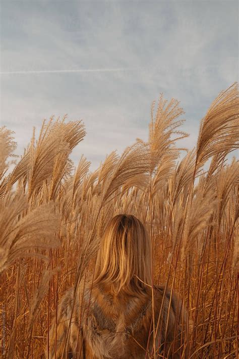 Red Haired Girl In A Fur Coat Stands In Tall Grass With Her Back To