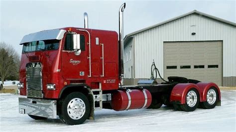 A Large Red Semi Truck Parked In Front Of A Building On A Snow Covered Field