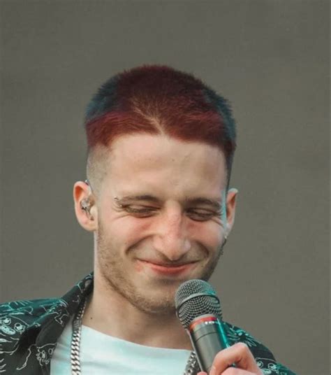 A Man With Red Hair And Piercings Holding A Microphone In Front Of His Face