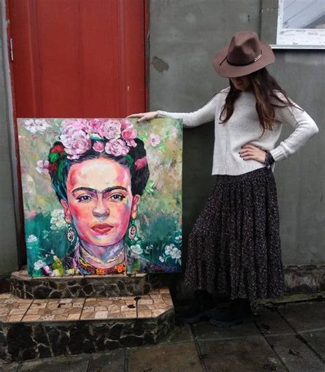 a woman standing next to a painting on the side of a building with a hat on her head