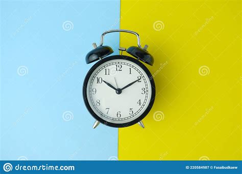 Reloj Despertador Negro Aislado Sobre Fondo Amarillo Y Azul Imagen De