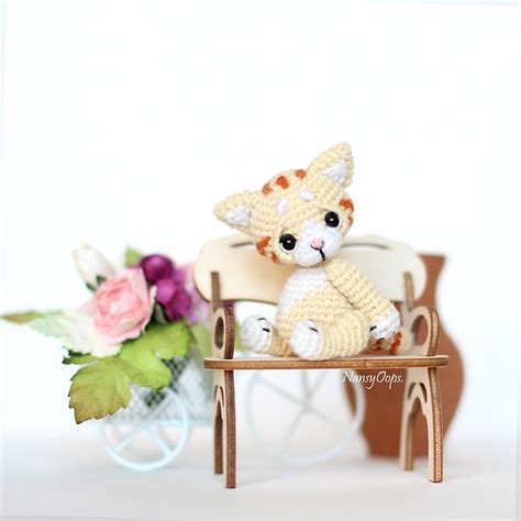 A Small Crocheted Cat Sitting On Top Of A Wooden Table Next To Flowers