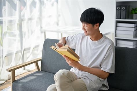 Premium Photo Relaxed Asian Man Enjoys Reading A Book On A Sofa In His Modern Living Room