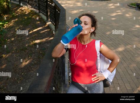 Attractive Thirsty Hispanic Fit Brunette In Tight Sportswear And With Ponytail Standing In A