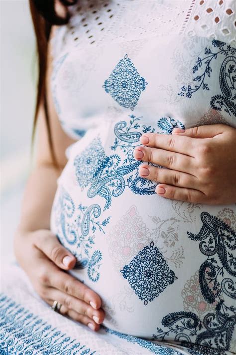 A Pregnant Woman Dressed In White Dress With Ornament Touches Her Belly