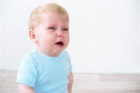 Premium Photo Blonde Baby In Blue Shirt Crying Sitting On Floor At Home