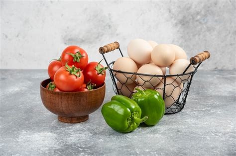 Cesta de mimbre de huevos orgánicos crudos pimientos y tomates rojos