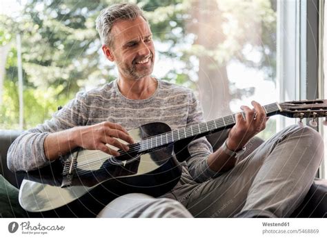 Happy Mature Man Lying On Couch At Home Playing Guitar A Royalty Free