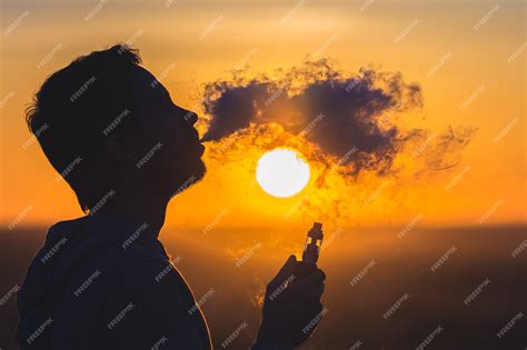 Premium Photo The Man Smoke An Electric Cigarette On The Sunset Backround