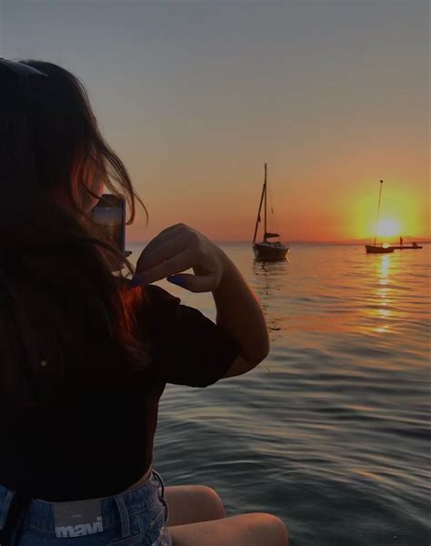 A Woman Sitting On The Beach Taking A Photo With Her Cell Phone As The