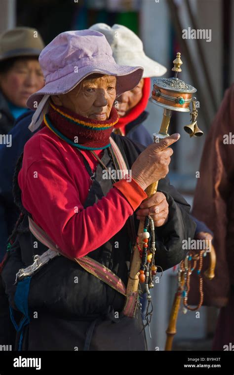 Tibetan Woman Pilgrim In Pink Hat Spinning Large Prayer Wheel In The