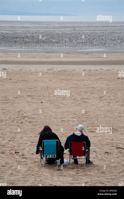 Couple Sitting In Deckchairs On The Beach At Low Tide In Weston Super