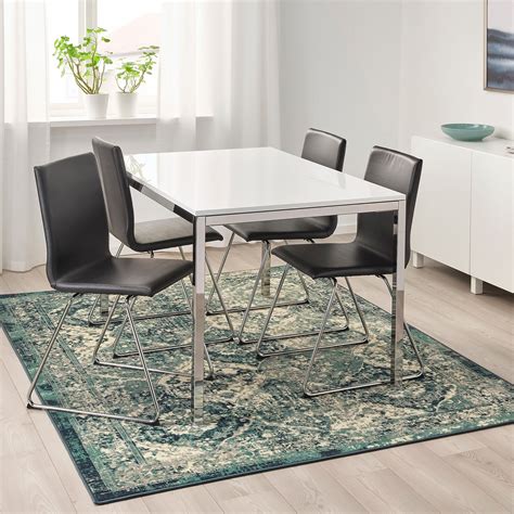 a white table with four black chairs on top of a blue rug in front of a ...