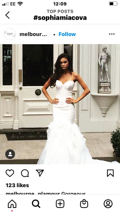 A Woman In A White Wedding Dress Standing Next To A Building