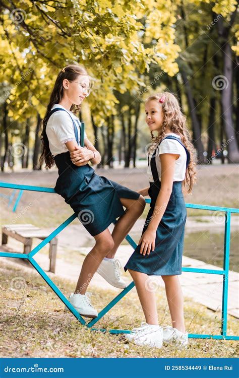 Two Schoolgirls in School Uniform are Walking in the Park on a Warm Day