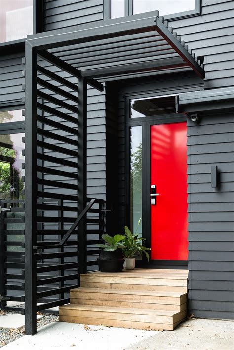 The black exterior of this home with a bold red front door hides a